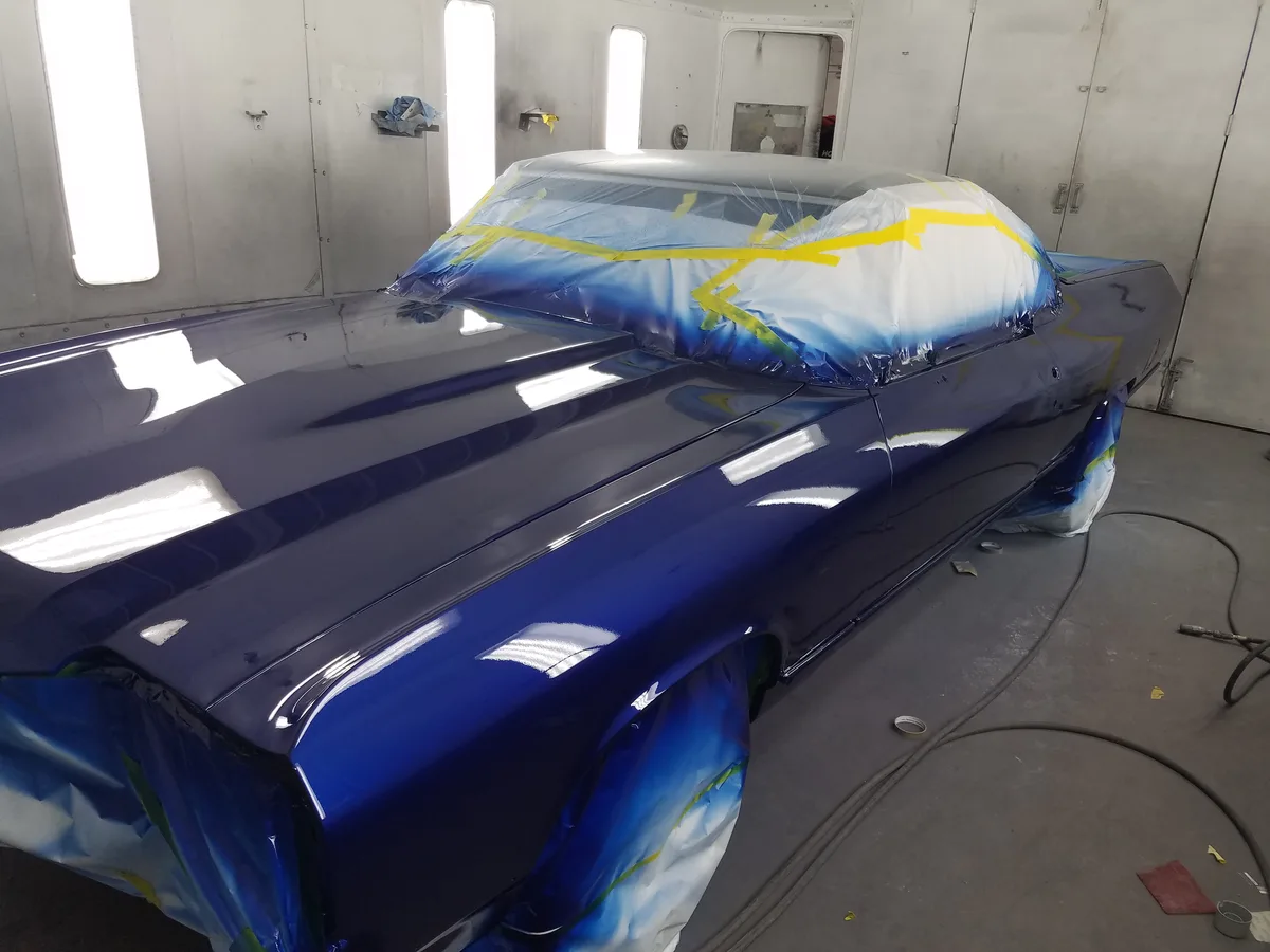 Same classic car with fresh deep blue paint finish in spray booth
