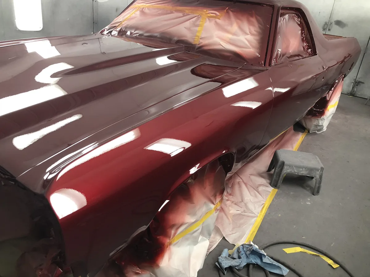 Classic car body with reflective burgundy paint in spray booth